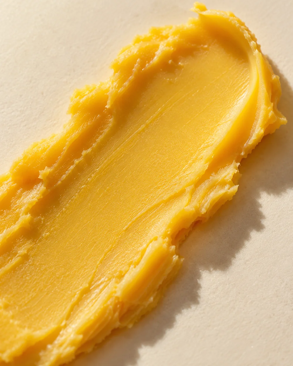 Studio della texture: un tratto di balsamo dorato, denso e burroso, con morbidi solchi sulla superficie.